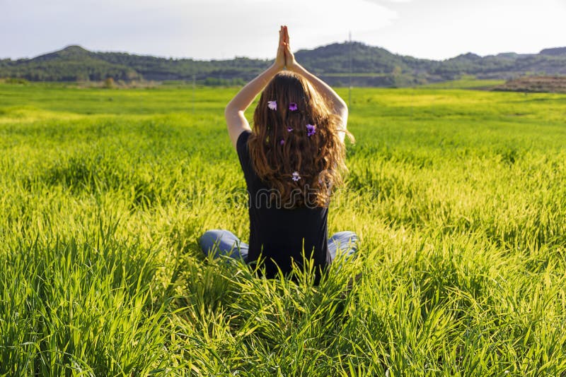 Young caucasian woman red-haired with freckles, resting on a green field at spring sunset, sitting in a yoga position. Meditation, mindfulness, relax. Young caucasian woman red-haired with freckles, resting on a green field at spring sunset, sitting in a yoga position. Meditation, mindfulness, relax