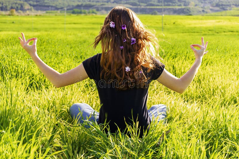 Young caucasian woman red-haired with freckles, resting on a green field at spring sunset, sitting in a yoga position. Meditation, mindfulness, relax. Young caucasian woman red-haired with freckles, resting on a green field at spring sunset, sitting in a yoga position. Meditation, mindfulness, relax