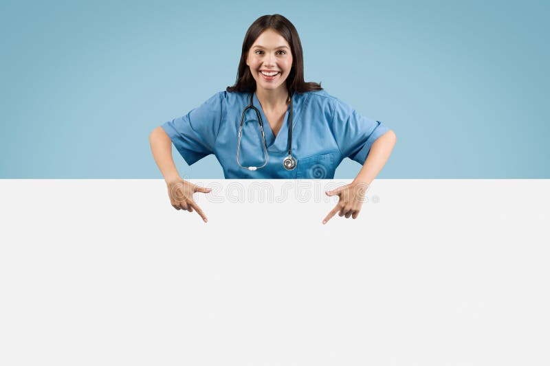 Junge Krankenschwester in blauem Mantel, die auf die weiße blaue Kulisse zeigt stockbild