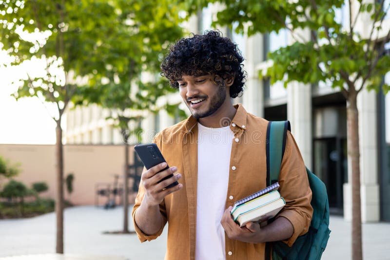 Junge lächelnde indische männliche Studentin kam, um außerhalb der Universität zu studieren und telefonisch zu telefonieren. Er hi stockfotos