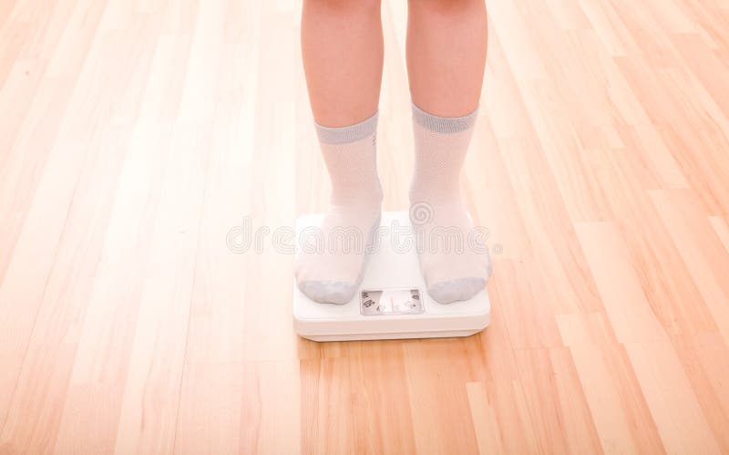 Boy measures weight on floor scales. Legs in socks standing at floor scales om hardwood floor in living room. Boy measures weight on floor scales. Legs in socks standing at floor scales om hardwood floor in living room.