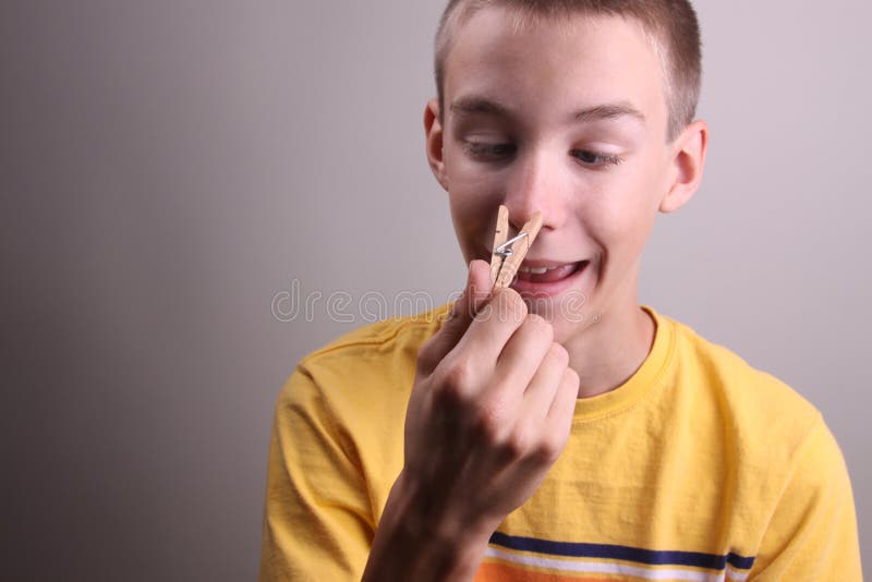 A young boy pinching his nose with a clothespin, and making a funny face. A young boy pinching his nose with a clothespin, and making a funny face.