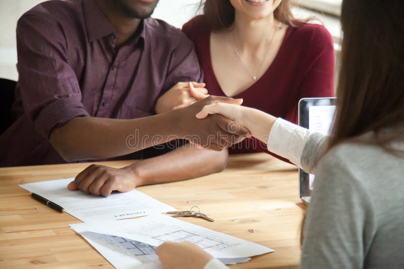 Junge multiethnische Paare, die Hände mit Immobilienagentur rütteln lizenzfreie stockbilder Junge multiethnische Paare, die Hände mit Immobilienagentur rütteln lizenzfreie stockbilder