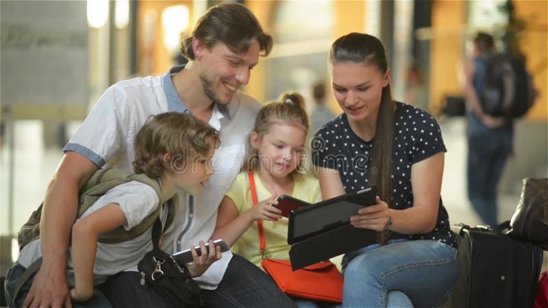 Junge Mutter, die ihrer Familie etwas interessant im Tablet-PC zeigt, während sie im Flughafenabfahrtaufenthaltsraum sitzen