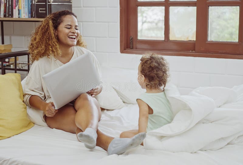 Junge Mutter, die Laptop benutzt, neben der Rolle von Tochter im Bett lizenzfreies stockfoto