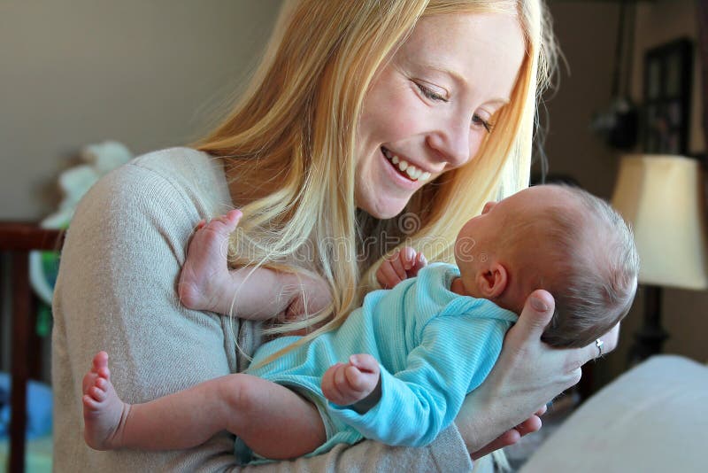 Junge Mutter, die am neugeborenen Baby in der Hauptkindertagesstätte lächelt stockbilder