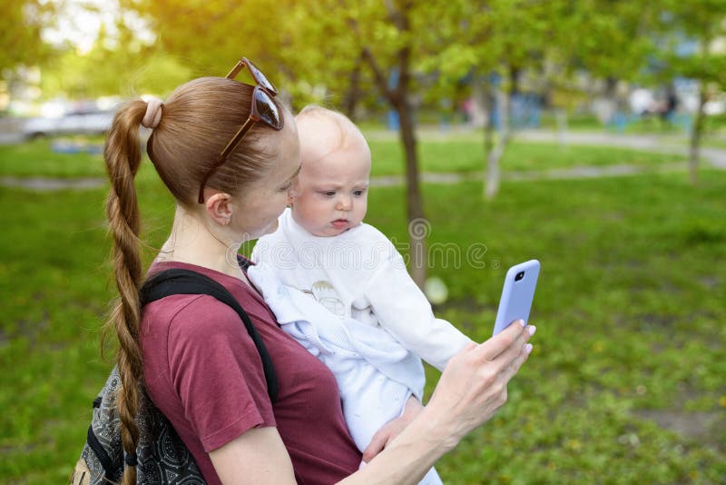 Junge Mutter mit einem Baby in ihren Armen und in Gebrauch ein Smartphone Selfie mit einem Kind Holland, Keukenhof stockfotografie Junge Mutter mit einem Baby in ihren Armen und in Gebrauch ein Smartphone Selfie mit einem Kind Holland, Keukenhof stockfotografie