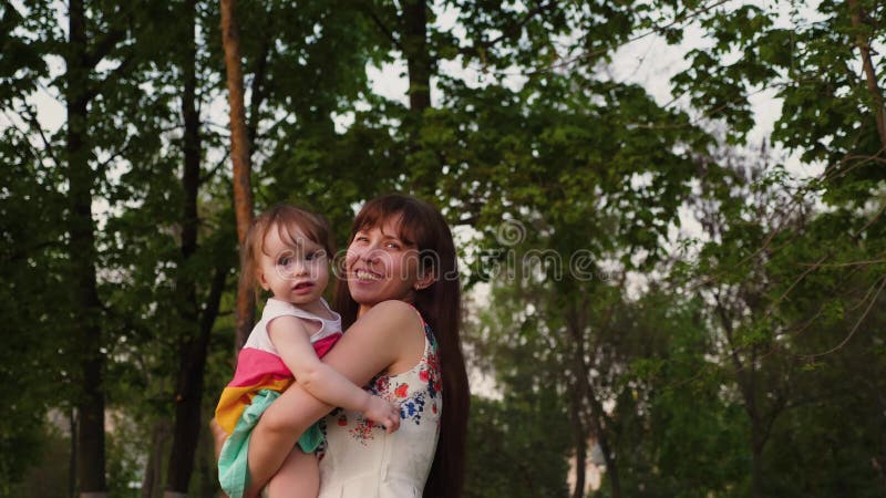 Junge Mutter spielt im Park mit einem kleinen Baby, das ihn in ihren Armen lacht und rüttelt
