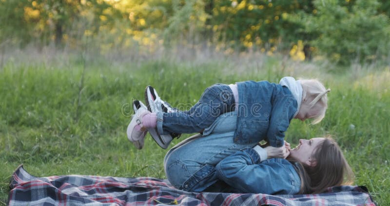 Junge Mutter spielt mit ihrer kleinen Tochter auf Picknick im Park. mädchen fliegt auf mutter füße.