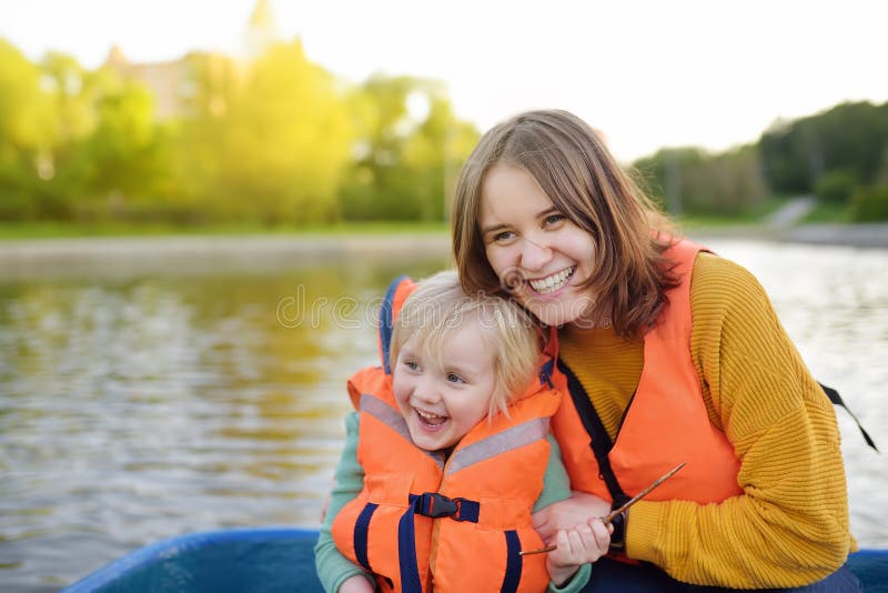 Junge Mutter und wenig Sohnbootfahrt auf einem Fluss oder einem Teich am sonnigen Sommertag Qualitätsfamilienzeit zusammen auf Na