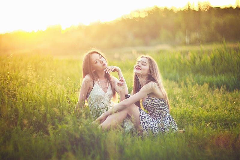 Junge Mädchen, die auf Gras in den Sonnenstrahlen und -unterhaltung sitzen stockfotos