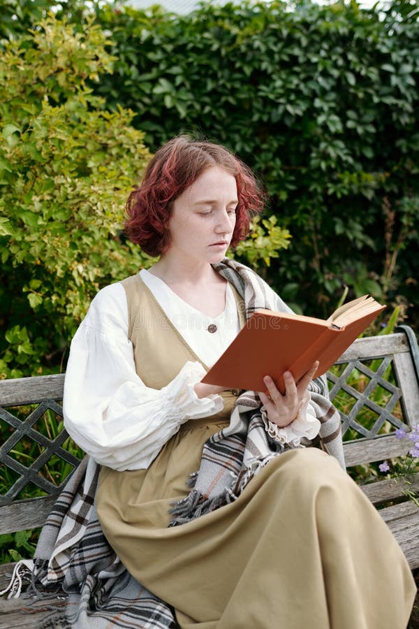 Junge Mädchen, die sich beim Lesen eines Buches über Opferkleidung auf einer Bank im Garten aufhalten lizenzfreies stockbild