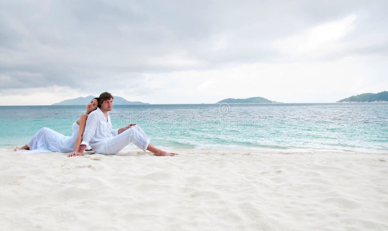 Junge Paare, die auf dem Strand nahe der Küste sitzen lizenzfreie stockfotos Junge Paare, die auf dem Strand nahe der Küste sitzen lizenzfreie stockfotos
