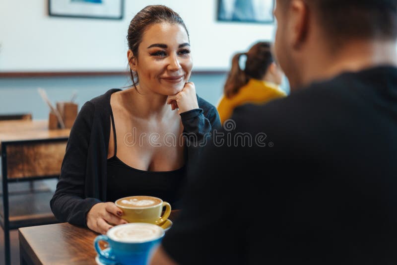 Junge Paare, die im Café am Datum, an trinkendem Kaffee sitzen und Nachtisch essen lizenzfreie stockbilder