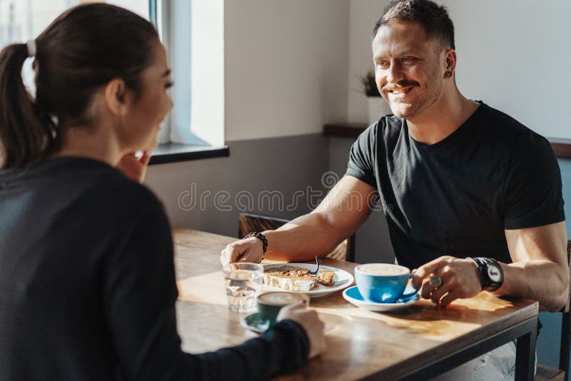 Junge Paare, die im Café am Datum, an trinkendem Kaffee sitzen und Nachtisch essen lizenzfreies stockfoto