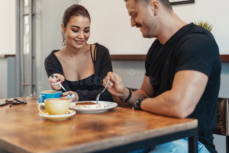 Junge Paare, die im Café am Datum, an trinkendem Kaffee sitzen und Nachtisch essen stockfoto