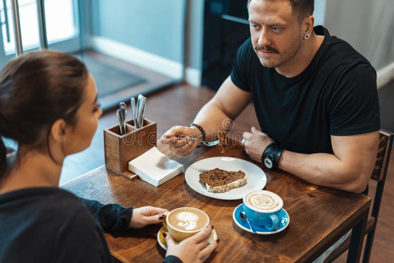 Junge Paare, die im Café am Datum, an trinkendem Kaffee sitzen und Nachtisch essen stockfotos