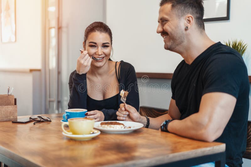 Junge Paare, die im Café am Datum, an trinkendem Kaffee sitzen und Nachtisch essen lizenzfreies stockfoto