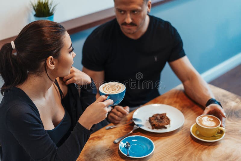 Junge Paare, die im Café am Datum, an trinkendem Kaffee sitzen und Nachtisch essen stockbild
