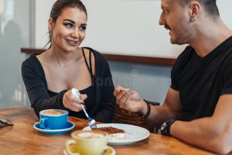 Junge Paare, die im Café am Datum, an trinkendem Kaffee sitzen und Nachtisch essen stockfoto