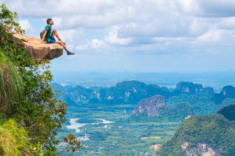Junge Reisende sitzen auf einem Felsen, der den Abgrund überragt, mit einer schönen Landschaft - Khao Ngon Nak Nature Trail in Kr stockfoto