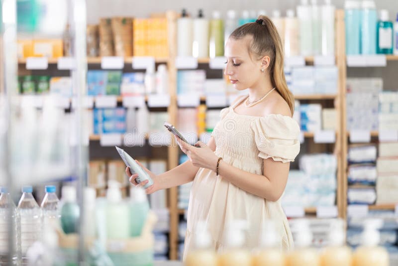 Junge Schwangere in Apotheken scannt QR-Code auf Körperbalsam stockbild