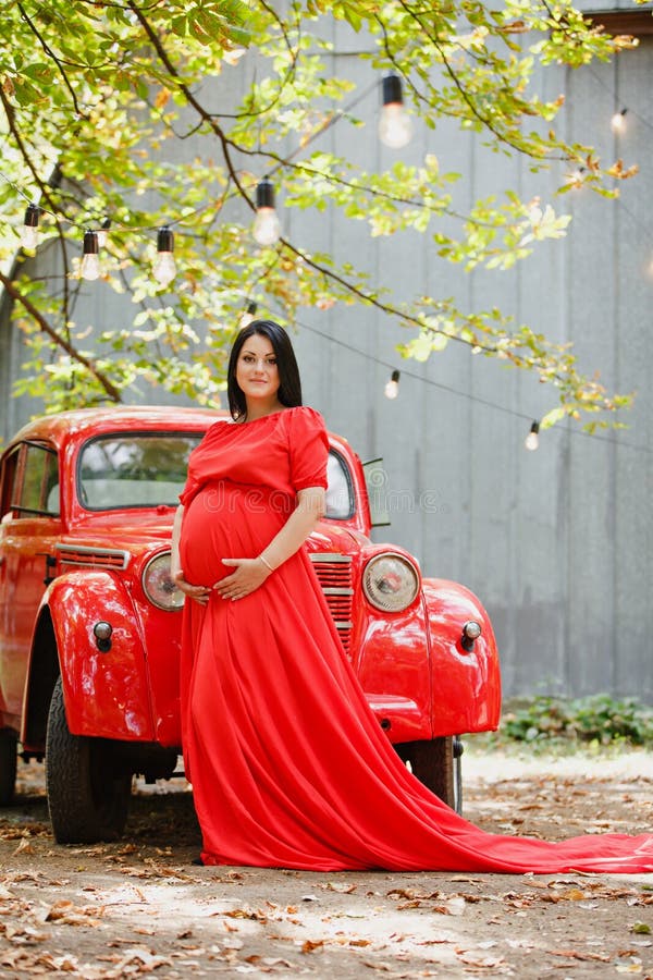 Junge schwangere Frau in einem Herbstgarten nahe rotem Retro- Auto lizenzfreies stockfoto Junge schwangere Frau in einem Herbstgarten nahe rotem Retro- Auto lizenzfreies stockfoto
