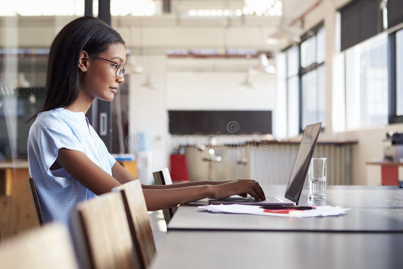 Junge schwarze Frau, die im Büro unter Verwendung einer Laptop-Computers arbeitet stockbilder