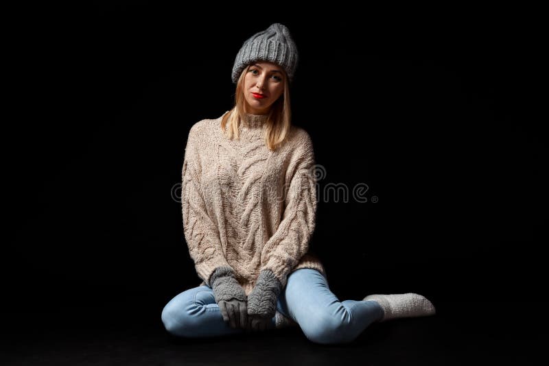 Junge schöne Blondine in gestrickten Handschuhen und in Hut im Grau, Blue Jeans, beige Strickjacke sitzen auf dem Boden mit den g lizenzfreie stockbilder Junge schöne Blondine in gestrickten Handschuhen und in Hut im Grau, Blue Jeans, beige Strickjacke sitzen auf dem Boden mit den g lizenzfreie stockbilder