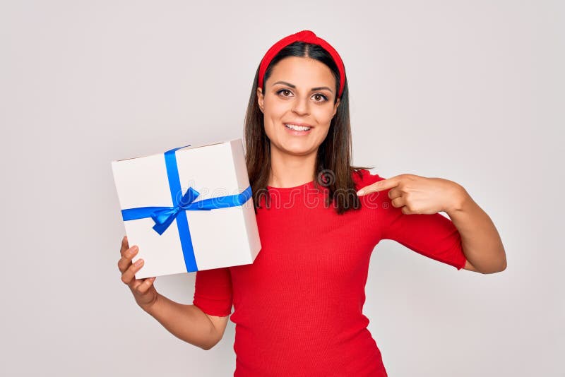 Junge schöne brunette Frau, die Geburtstagsgeschenk über isolierten weißen Hintergrund hält und mit dem Finger auf ein sich selbst lizenzfreie stockfotos