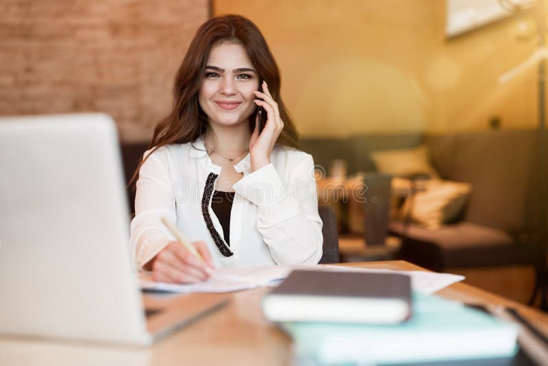 Junge schöne Frau, die in ihrem Laptop arbeitet und am Telefon spricht, während sie im Café zu Mittag im Multitasking der moderne stockfotos Junge schöne Frau, die in ihrem Laptop arbeitet und am Telefon spricht, während sie im Café zu Mittag im Multitasking der moderne stockfotos