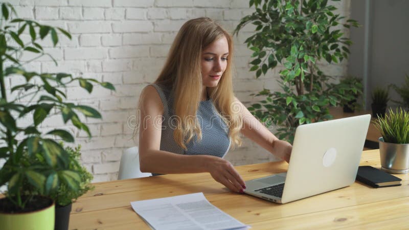 Junge schöne Geschäftsfrau, die am Tisch mit Laptop sitzt