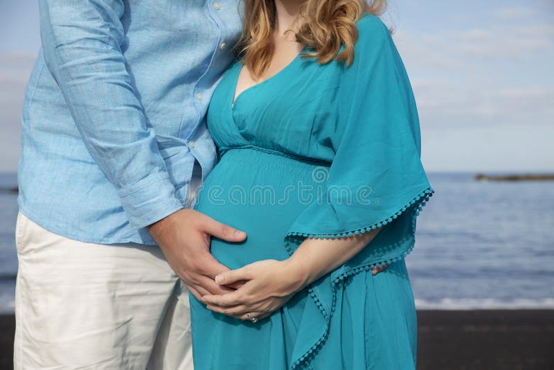 Junge schöne Paare am Ozean, Mann, der den schönen runden Tummy der schwangeren Frau hält lizenzfreies stockbild Junge schöne Paare am Ozean, Mann, der den schönen runden Tummy der schwangeren Frau hält lizenzfreies stockbild