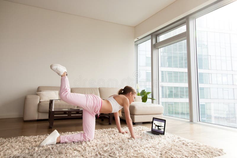 Young sporty woman working out at home, teenager doing fitness exercises on living room floor for buttocks legs shaping using online personal training program, doing yoga pilates indoors, copy space. Young sporty woman working out at home, teenager doing fitness exercises on living room floor for buttocks legs shaping using online personal training program, doing yoga pilates indoors, copy space