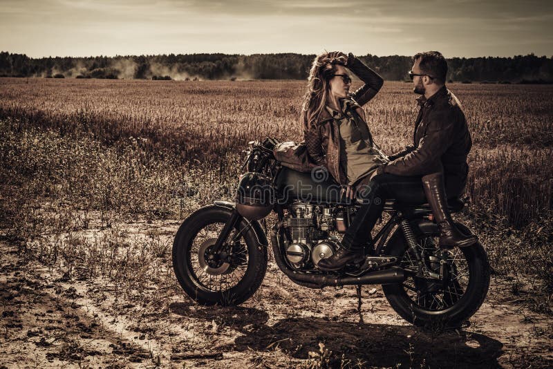 Junge, stilvolle Caférennläuferpaare auf kundenspezifischen Motorrädern der Weinlese auf dem Gebiet stockfotografie Junge, stilvolle Caférennläuferpaare auf kundenspezifischen Motorrädern der Weinlese auf dem Gebiet stockfotografie