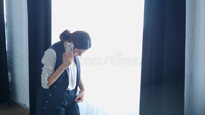 Junge stolze Geschäftsfrau spricht an ihrem Handy mit Kunden, bei der Stellung des nahen Bürofensters lizenzfreie stockbilder