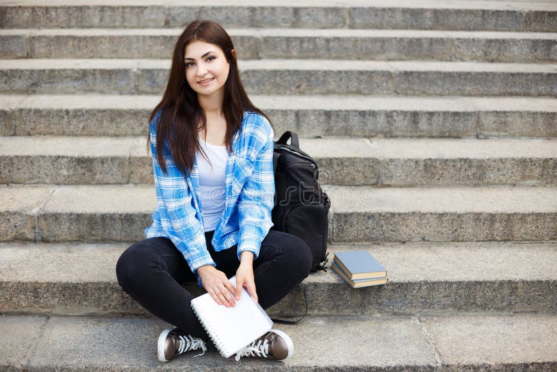 Junge Studentenfrau, die auf der Stadttreppe mit einem Buch in ha sitzt stockfotografie Junge Studentenfrau, die auf der Stadttreppe mit einem Buch in ha sitzt stockfotografie