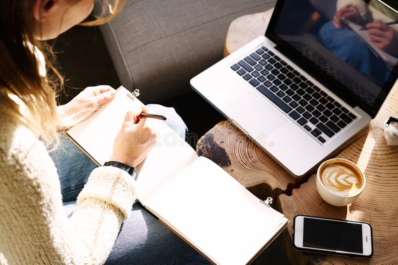 Junge Studentin, die Kaffee im sonnigen Café arbeitet und schreibt an geöffnetem Laptop und trinkt stockfoto
