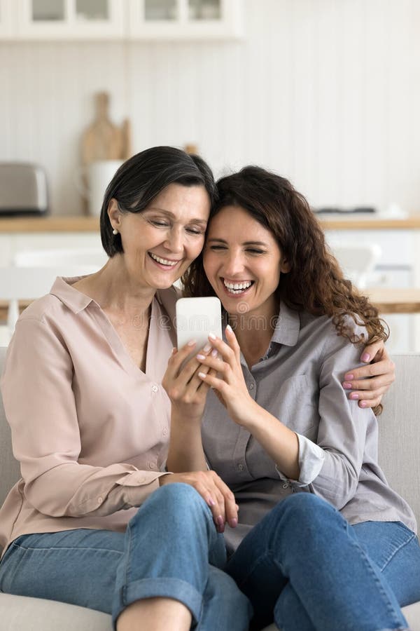 Junge Tochter lachend ältere Mutter, die telefonisch auf Sofa kuschelt lizenzfreies stockbild