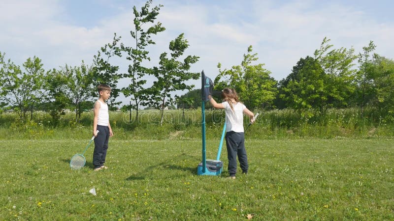 Junge und Mädchen des jungen jugendlich, die Badminton in der Wiese mit Wald im Hintergrund spielen Kinder mit Federballschlägern