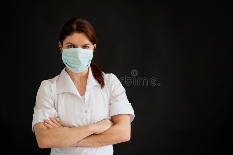 Junge Ärztin in Uniform in einer medizinischen Maske auf einem schwarzen Hintergrund. eine Krankenschwester in einem Kaufhaus falt