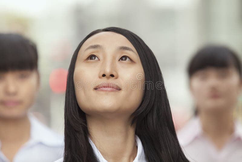 Junge überzeugte Geschäftsfrau Looking oben, draußen mit Leuten im Hintergrund stockfotografie Junge überzeugte Geschäftsfrau Looking oben, draußen mit Leuten im Hintergrund stockfotografie