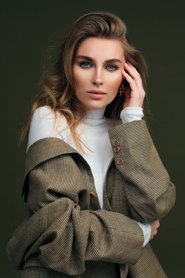 Jungen schönen Blondine in einem weißen Schildkrötenhals und in einem a Mensch Jackenhaltungen auf einem grünen Oliven Hintergrund stockfotografie