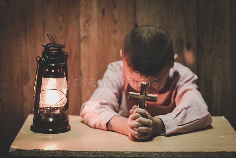 Jungenhände, die ein heiliges Kreuz betet zum Gott in der Dunkelheit und mit der Lampe dazu, Kind betet für Gott-Religion halten lizenzfreie stockfotografie Jungenhände, die ein heiliges Kreuz betet zum Gott in der Dunkelheit und mit der Lampe dazu, Kind betet für Gott-Religion halten lizenzfreie stockfotografie