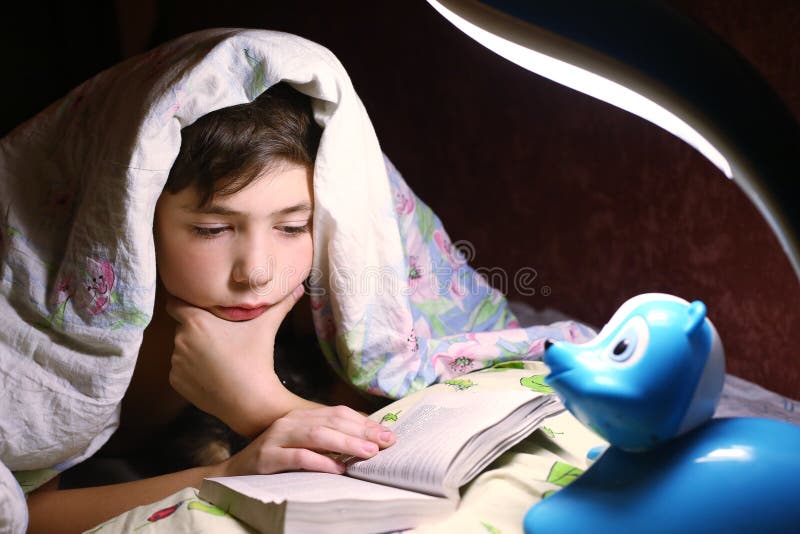 Jungenlesebuch unter der Decke in der Nachtstunde lizenzfreie stockbilder Jungenlesebuch unter der Decke in der Nachtstunde lizenzfreie stockbilder