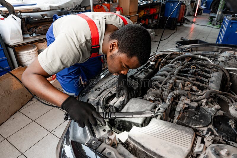Junger afrikanischer Automechaniker, der den Motor unter der Motorhaube im Auto-Service überprüft lizenzfreies stockfoto