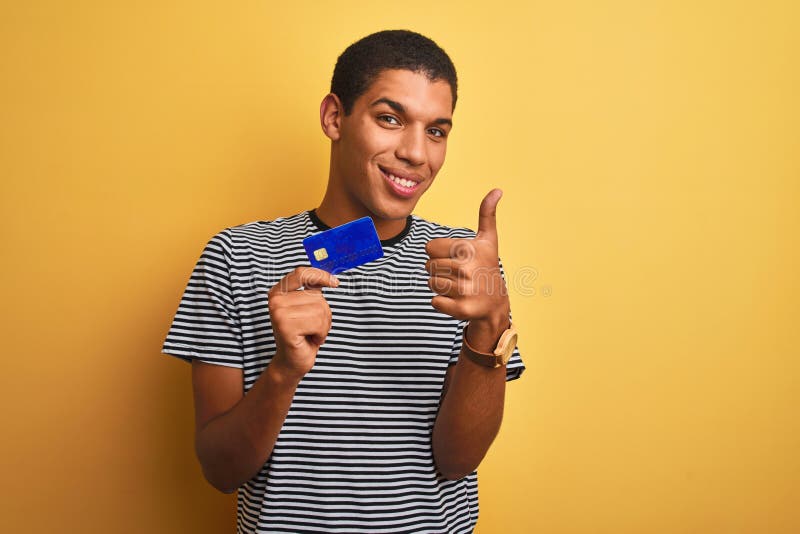 Junger arab Mann mit Kreditkarte über isoliertem gelbem Hintergrund glücklich mit einem großen Lächeln und macht sich ein Bild lizenzfreies stockbild