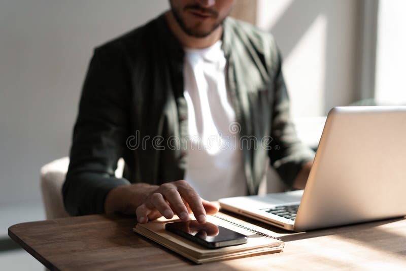Junger Arbeitnehmer am Arbeitsplatz, der über das Mobiltelefon die sozialen Medien auf dem Smartphone abfragt und dabei den Schrei stockfoto