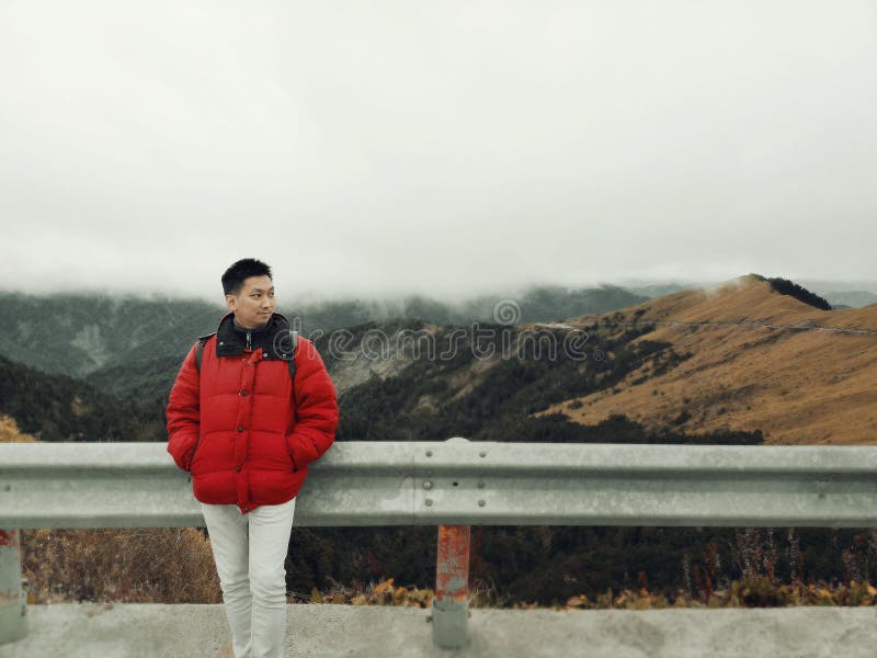 Junger asiatischer Mann, der im Wind und im Nebel auf die Gebirgsoberseite mit schöner Landschaft im Hintergrund genießt lizenzfreie stockbilder Junger asiatischer Mann, der im Wind und im Nebel auf die Gebirgsoberseite mit schöner Landschaft im Hintergrund genießt lizenzfreie stockbilder