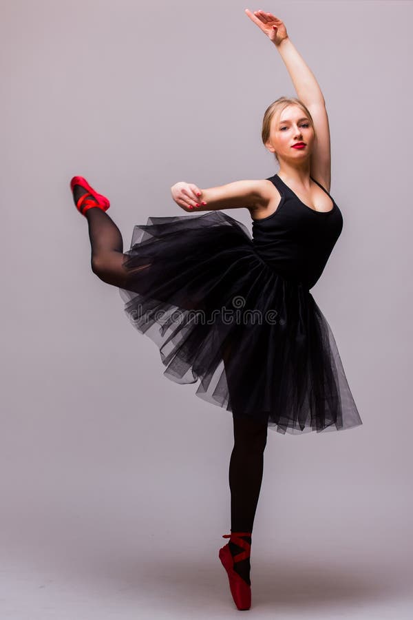 Junger blonder Ballerinamädchentanz und Aufstellung in den schwarzen Ballettröckchen- und Ballettschuhen auf grauem Hintergrund stockfotografie Junger blonder Ballerinamädchentanz und Aufstellung in den schwarzen Ballettröckchen- und Ballettschuhen auf grauem Hintergrund stockfotografie
